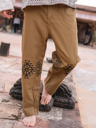 A person in 100% cotton Tribal pants with black geometric designs walks barefoot on stone pavement, with blurred figures and structures in the background.