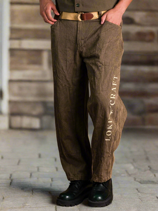 A person wearing Chopper Pants featuring LOKY-CRAFT text on the left leg, paired with a tan belt and black boots, stands on a stone floor against a wooden background.