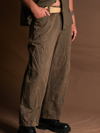 Wearing vintage Chopper Pants in a subtle stonewash with a matching shirt and black boots, a person stands against a brown background. Only the lower torso and legs are shown.
