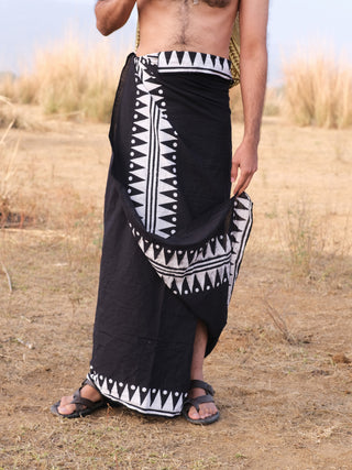 Outdoors on dry grass, a person wears a black Jiva Dhoti—a traditional Indian garment—with sandals. Their upper body is bare and their face isnt visible.