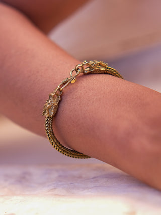 A close-up of the Takshaka Bracelet on a wrist reveals its intricately designed animal head clasps and woven chain, set against a blurred background to highlight its exquisite details.