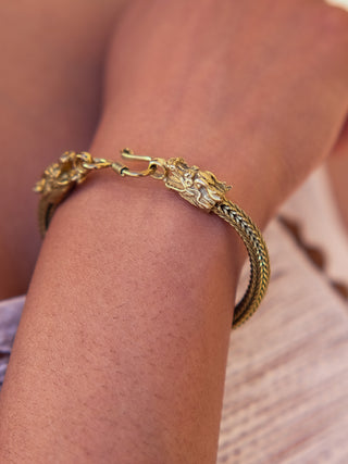 A close-up shows a wrist wearing the Takshaka Bracelet, highlighting intricate dragon head designs at each end and a visible clasp. The textured, braided appearance stands out against a blurred background, emphasizing the premium quality of this stylish accessory.