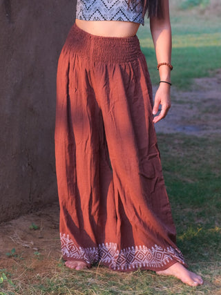A person stands barefoot outdoors, their lower body visible and styled in Medusa Palazzo Pants with a white geometric pattern, paired with a patterned crop top for a boho-chic vibe.