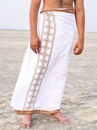 A person barefoot on sand wears a Kangura Dhoti in white and brown, decorated with traditional Rajasthani handblock geometric prints on 100% cotton, enhancing the serene cultural vibe under a clear sky.