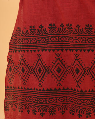 Close-up of Vasuki dhoti showcasing red fabric adorned with intricate black geometric and floral patterns, similar to Rajasthani handblock prints with diamond shapes and decorative borders. The visible texture reveals its soft, flowy material.